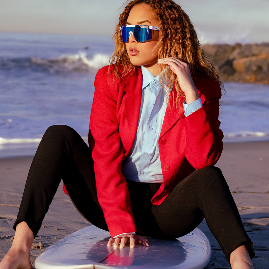 / Polarized Blue | Woman posing on surfboard wearing Pit Viper Sunglasses